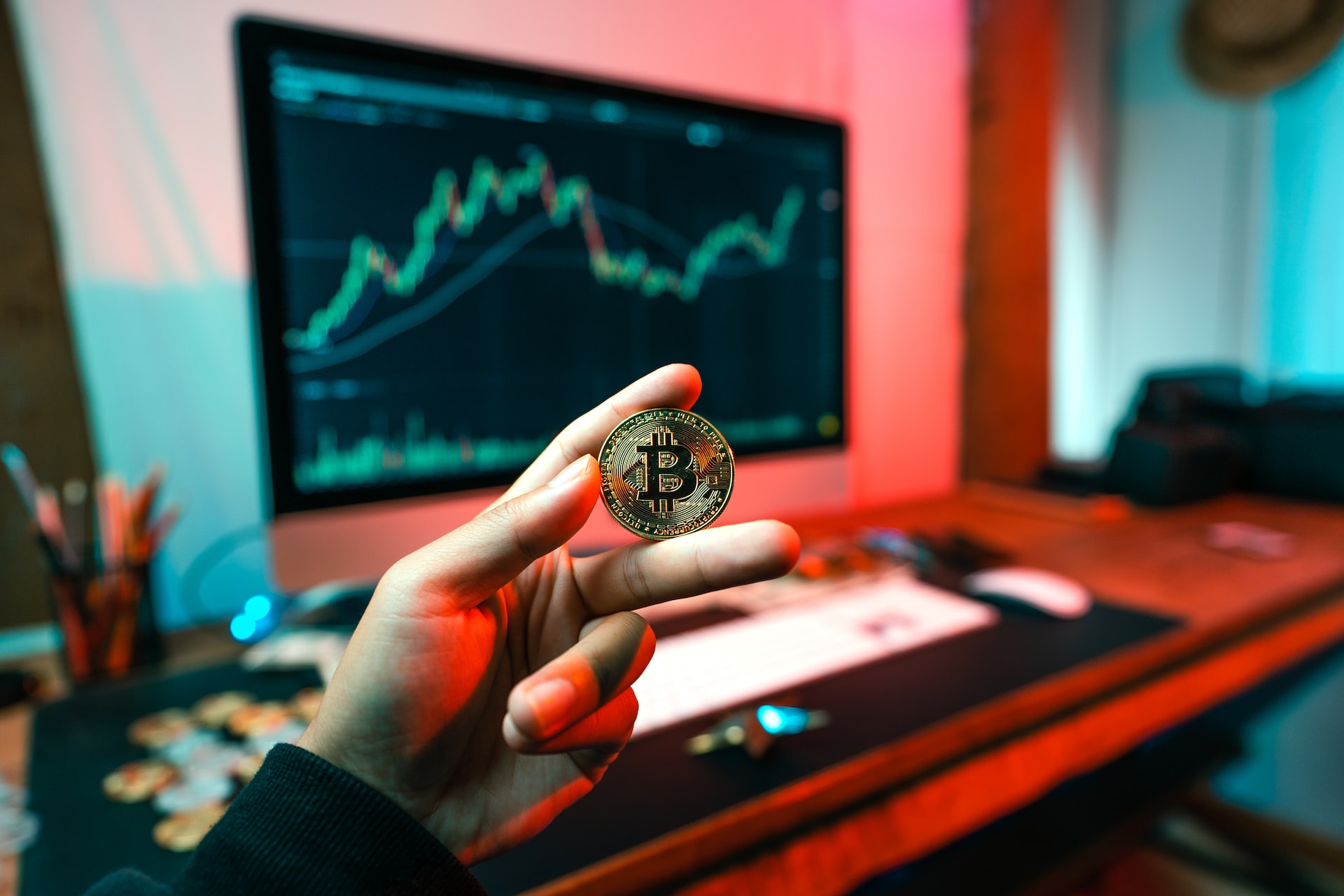 A close-up picture of a person holding a bitcoin in their hand with a computer in the background.